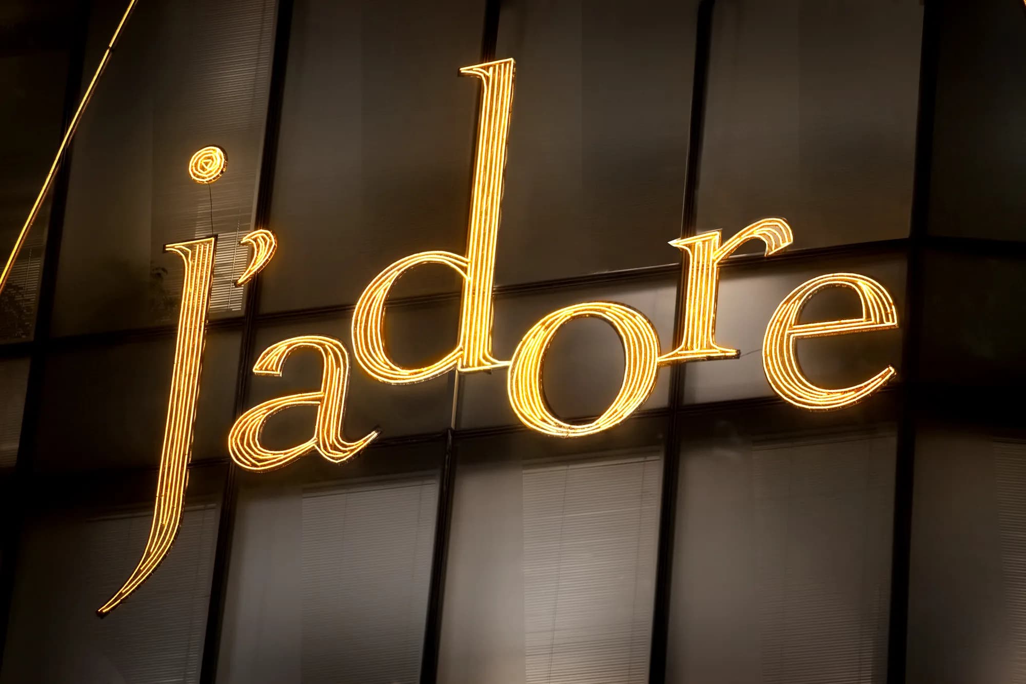 Illuminated gold J'adore lettering across the Dior 57th Street facade at night