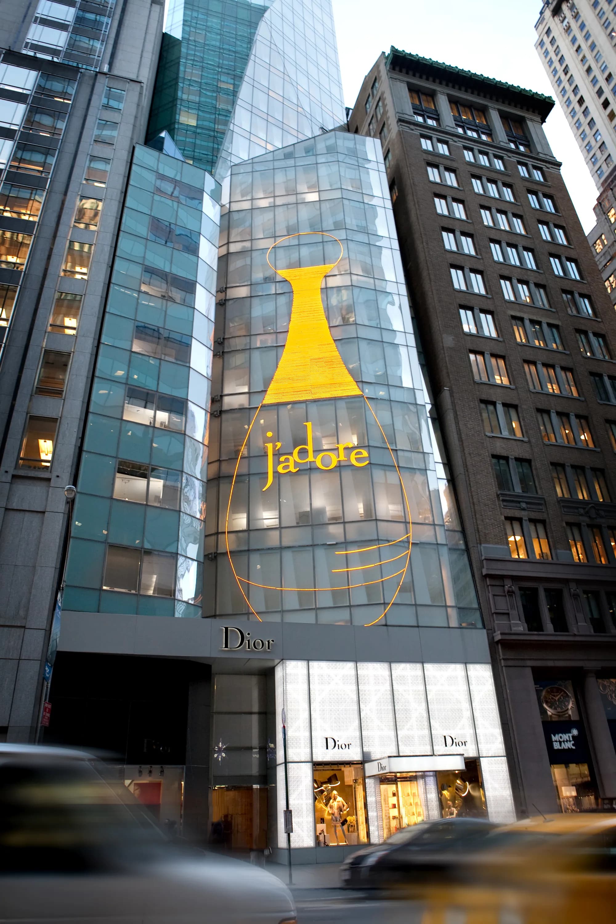 Dior 57th Street tower at dusk with the gold J'adore bottle facade above the boutique entrance