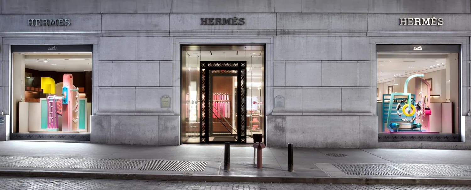 Hermès storefront at night with three windows of pastel sculptural installations