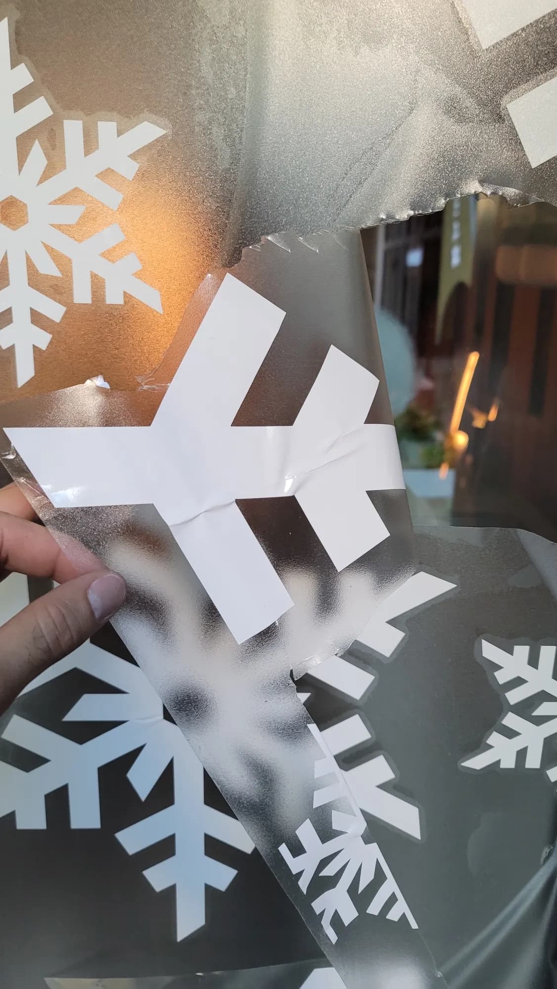 Installer's hand applying a frosted snowflake vinyl decal to Panerai window glass